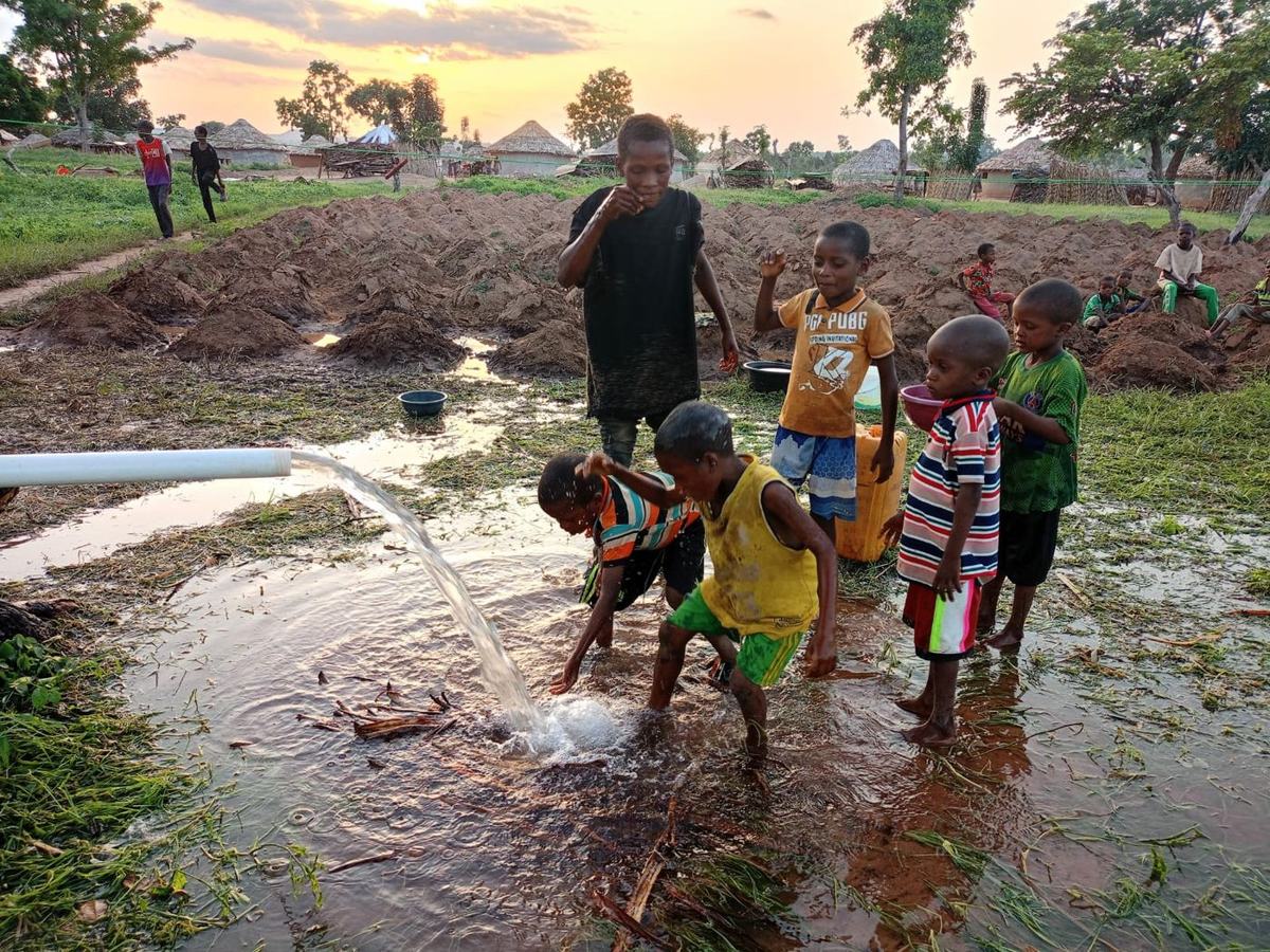 Village children splashing in water flowing from a newly tested well at sunset